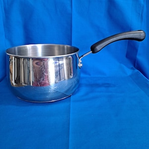 Può includere: Una casseruola in acciaio inossidabile con manico nero. La pentola ha una superficie lucida e riflettente ed è posta su uno sfondo blu. Il manico è curvo per una facile presa. Questa pentola è ideale per cucinare.