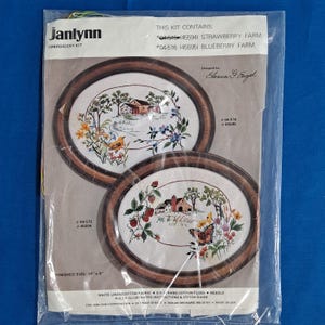 May include: A vintage embroidery kit featuring two oval-shaped designs, one with a strawberry farm and the other with a blueberry farm. The kit includes white linen fabric, six-strand cotton floss, a needle, and fully illustrated instructions. The finished size is 10 inches by 8 inches.