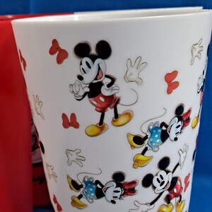 Puede incluir: Vaso blanco con personajes de dibujos animados de Mickey Mouse y Minnie Mouse. El vaso tiene un interior rojo y est&aacute; decorado con lazos rojos y guantes blancos. El dise&ntilde;o incluye los pantalones cortos rojos y los zapatos amarillos de Mickey.