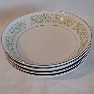 Puede incluir: Juego de cuatro cuencos de sopa de cerámica blanca con un patrón floral en tonos verdes, azules y rosas. Los cuencos tienen un borde plateado.