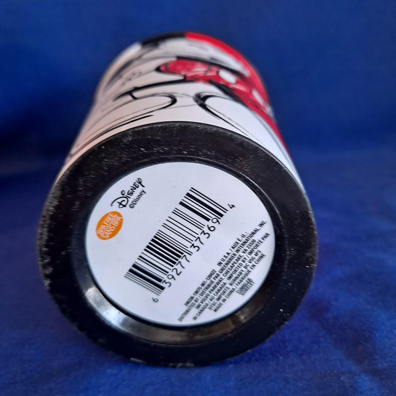 Puede incluir: Un vaso cil&iacute;ndrico con base y borde negros, con un cuerpo blanco con gr&aacute;ficos rojos y negros. El vaso tiene un c&oacute;digo de barras y el logotipo de Disney. Tambi&eacute;n se ven las palabras "Sin BPA".