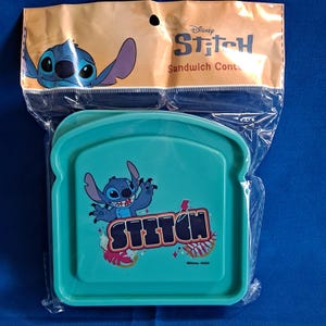May include: A teal sandwich container featuring the character Stitch from Disney's Lilo & Stitch. The container has a graphic of Stitch and the word "Stitch". The packaging is tan with a Stitch graphic and the words "Sandwich Cont."