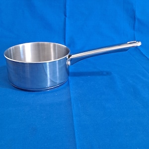 May include: A stainless steel saucepan with a polished finish, featuring a cylindrical body and a long, straight handle attached with a single visible rivet. The interior of the pan is smooth and metallic, showing a consistent brushed texture throughout.