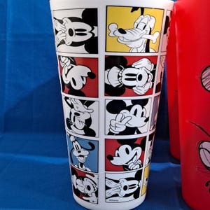 Puede incluir: Un vaso blanco con un dise&ntilde;o de c&oacute;mic que presenta a Mickey Mouse y Goofy en varias poses. Los paneles est&aacute;n enmarcados en rojo y amarillo, con un vaso rojo visible a la derecha.