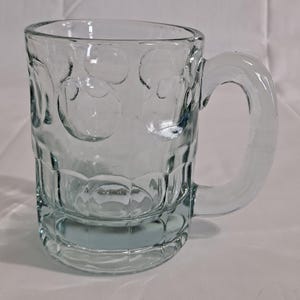 以下が含まれることがあります： テクスチャ加工されたデザインの透明なガラス製のマグカップ。マグカップにはハンドルと丸い底があります。
