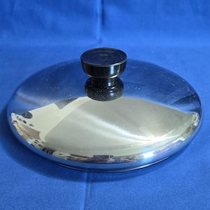 Peut inclure: Un couvercle de casserole circulaire en acier inoxydable poli doté d'une surface réfléchissante semblable à un miroir. Le couvercle est surmonté d'un bouton noir cylindrique centré, fabriqué dans un matériau lisse et solide.