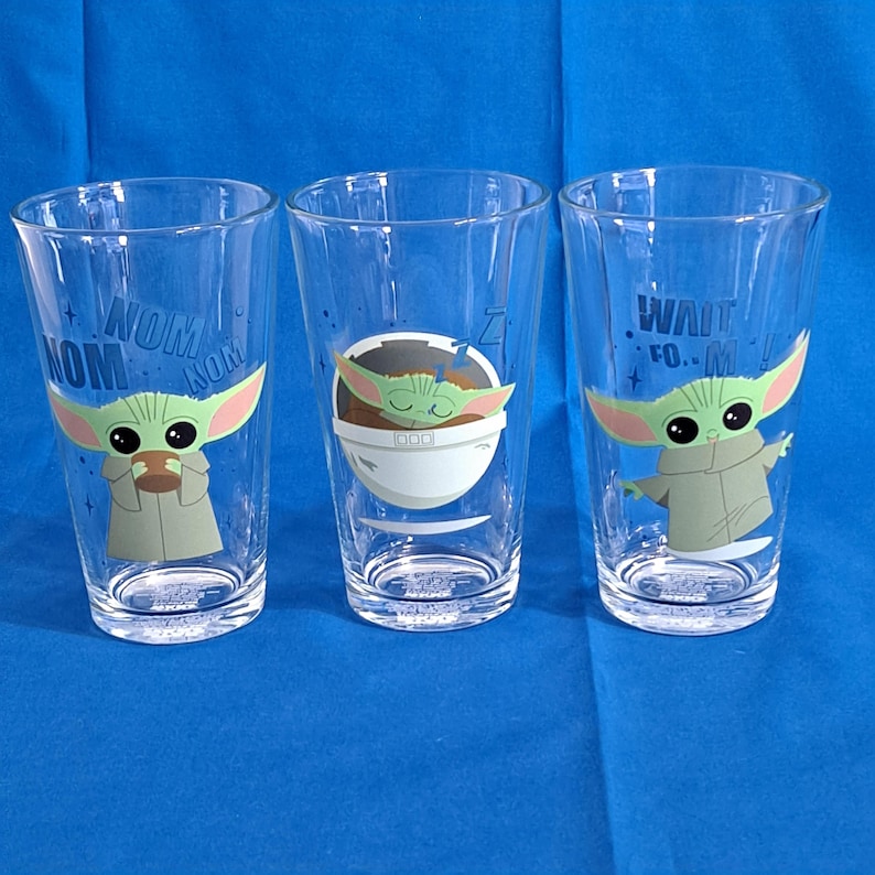 Peut inclure: Trois verres transparents avec le personnage Grogu de The Mandalorian. Chaque verre a un design diff&eacute;rent : l'un avec Grogu tenant une tasse et le texte "NOM NOM", un autre avec Grogu endormi, et le dernier avec Grogu tendant la main et le texte "WAIT FOR IT..."
