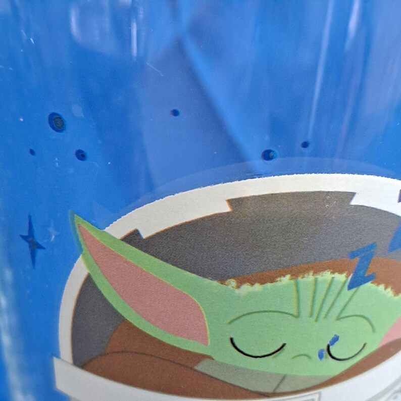 Peut inclure: Un gobelet en plastique bleu avec un dessin d'un personnage extraterrestre vert endormi avec de grandes oreilles. Le personnage porte une robe marron et a les yeux ferm&eacute;s. Le fond est bleu avec des &eacute;toiles blanches.