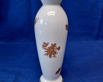 May include: A white ceramic vase with a gold rim and brown floral design. The vase has a slender, oval shape and a delicate floral pattern.
