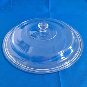 May include: A clear glass lid with a round knob on top. The lid is designed for a pot or pan.