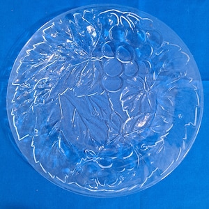 May include: A clear glass plate with a grapevine design. The plate features a raised design of grapes and leaves.