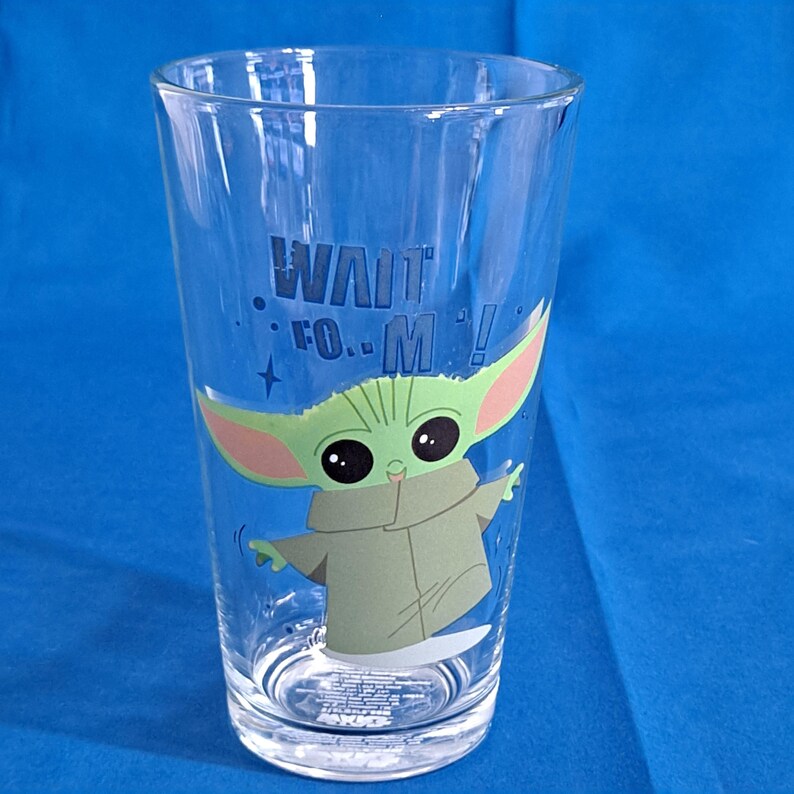 Peut inclure: Un verre transparent avec un personnage de dessin anim&eacute; vert et le texte "WAIT FOR M!". Le personnage a de grandes oreilles et porte un manteau beige. Le verre est cylindrique et est probablement utilis&eacute; pour boire des boissons.
