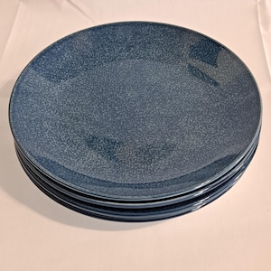 May include: A stack of four blue ceramic dinner plates with a speckled glaze.