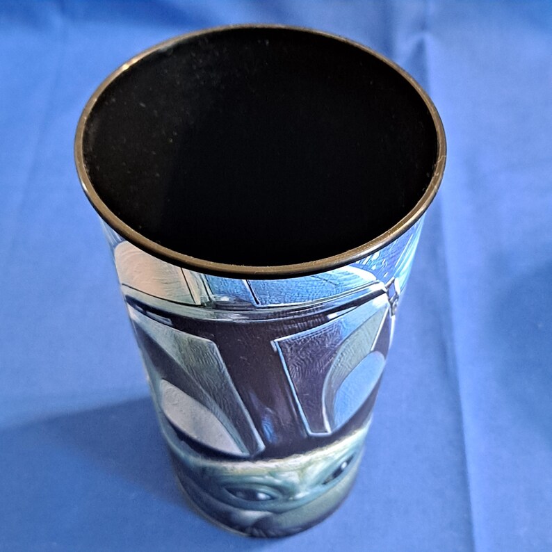May include: A tall, cylindrical tumbler with a black interior and a metallic gold rim. The exterior features a blue and silver design with a character from a popular science fiction franchise. The bottom of the tumbler features a green character.