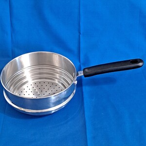 May include: A stainless steel steamer pot with a black handle. The pot has a perforated bottom and a circular design. The handle is ergonomically shaped for a comfortable grip. The pot is designed for steaming vegetables and other foods.