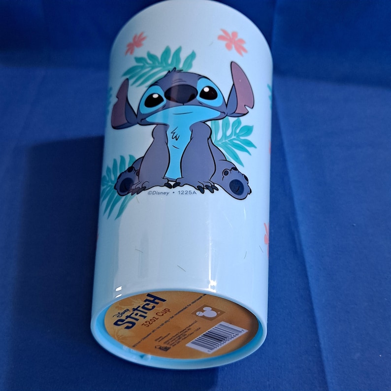 May include: A light blue 32oz Stitch cup featuring a cartoon image of Stitch surrounded by tropical leaves and flowers. The cup has a light blue background and a brown bottom.