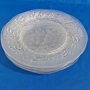 May include: A set of four clear glass dinner plates with a raised floral design and a textured surface.