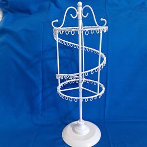 May include: White metal jewelry display stand with a spiral design. The stand has a round base and multiple tiers for displaying necklaces, bracelets, and earrings. The top features decorative swirls.