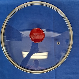 May include: A clear glass lid with a silver rim and a red knob with the word "T-fal" printed on it.