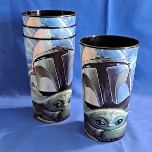 May include: Set of four tall plastic tumblers featuring a design of a Mandalorian helmet and Grogu, also known as Baby Yoda, against a blue and white background. The tumblers have a black rim and are suitable for cold beverages.