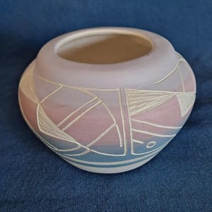May include: A small, round ceramic bowl with a wide opening. The bowl features a geometric design in white against a gradient of pink, blue, and lavender. The bowl is approximately 4 inches in diameter and 3 inches tall.
