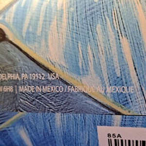May include: Close-up of a textile with a blue and white feather-like pattern. The text "DELPHIA, PA 19112 USA" and "MADE IN MEXICO / FABRIQUE AU MEXIQUE" is visible. The background is a mix of light blue and white.