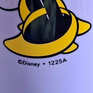 May include: Close-up of a yellow and black cartoon character design on a light purple background. The text "&copy;Disney &bull; 1225A" is printed below the design.