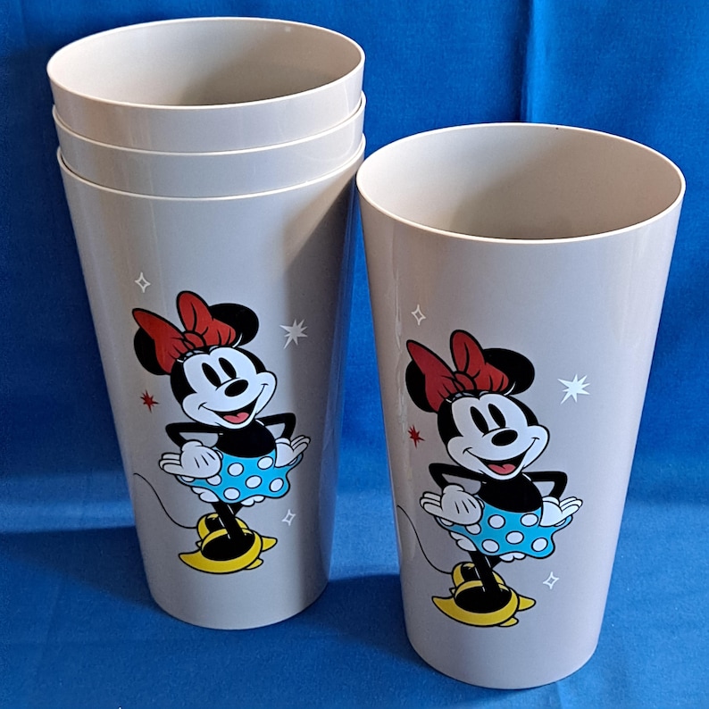 May include: Six grey plastic tumblers with a Minnie Mouse design. Each tumbler features a cartoon image of Minnie Mouse wearing a red bow, blue polka-dot skirt, and yellow shoes. The tumblers are decorated with star accents.