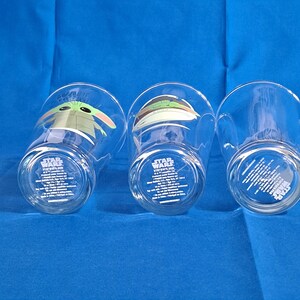 Peut inclure: Trois verres transparents repr&eacute;sentant des personnages de Star Wars. Chaque verre a un design diff&eacute;rent, dont le personnage Grogu. Les verres ont le logo Star Wars et du texte en bas.