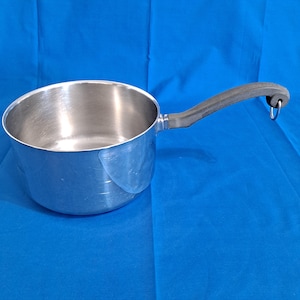 May include: A stainless steel saucepan with a black handle and a hanging loop. The pot has a shiny, reflective surface and is designed for cooking. The handle is ergonomically shaped for a comfortable grip.
