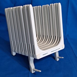 May include: A white and gray plastic bread slicing guide. The guide has multiple vertical slots for slicing bread evenly. The word "PRESTO" is printed on the front, along with "BREAD SLICING GUIDE".