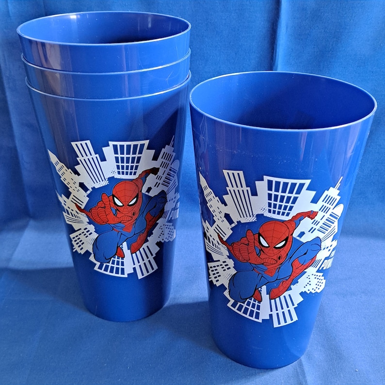 May include: Set of blue plastic cups featuring Spider-Man in a cityscape design. The cups have a tapered shape and a glossy finish. The Spider-Man graphic is in red, blue, and white.