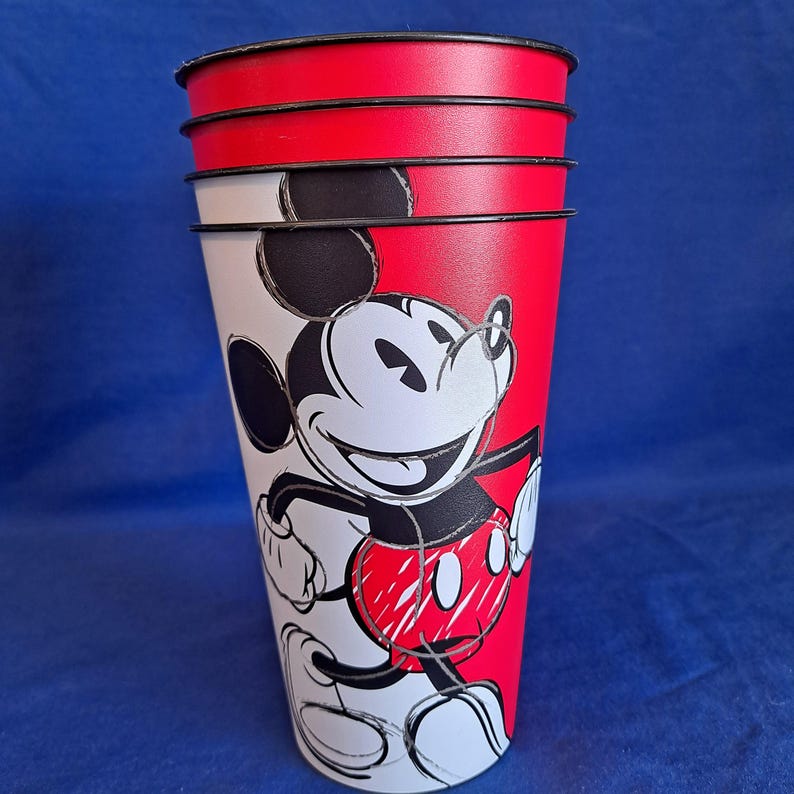 Puede incluir: Juego de cuatro vasos de Mickey Mouse rojos, blancos y negros. Cada vaso presenta una parte superior roja y un dise&ntilde;o dividido con la cara de Mickey. Los vasos est&aacute;n apilados, mostrando el ic&oacute;nico personaje.