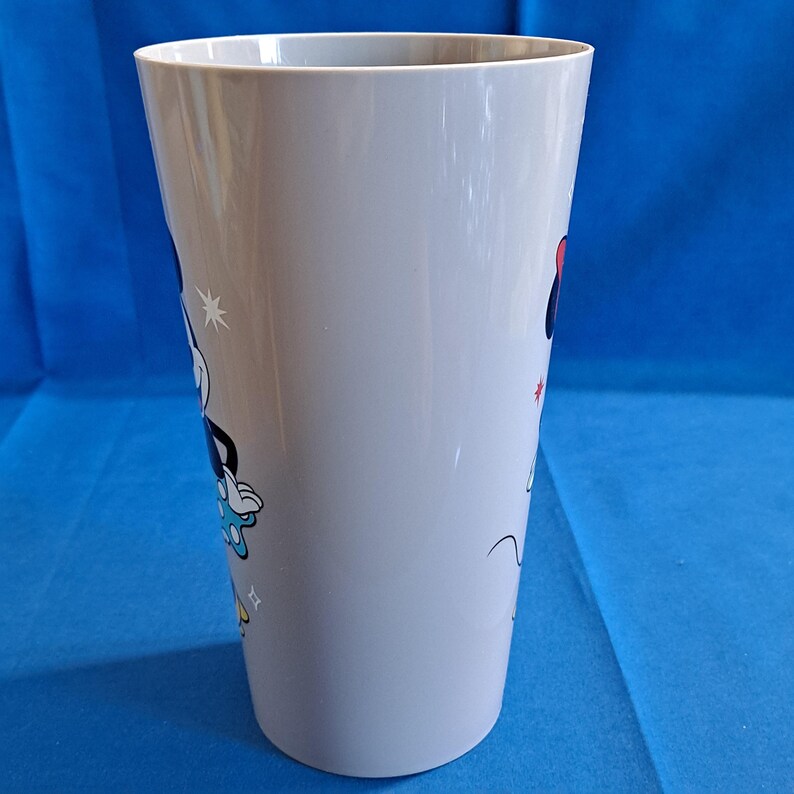 May include: A tall, light grey plastic tumbler featuring cartoon images of Mickey and Minnie Mouse. Mickey is wearing blue shorts and gloves, while Minnie sports a red bow. The tumbler has a wide opening and a slightly tapered shape.