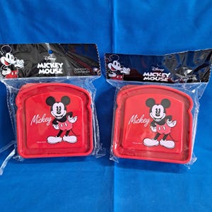 May include: Two red Mickey Mouse sandwich containers in clear plastic packaging. Each container has a Mickey Mouse graphic and the word "Mickey" in white. The packaging has the Disney Mickey Mouse logo.