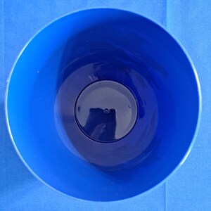 May include: A top-down view of a blue plastic container. The container is round with a dark blue interior and a lighter blue exterior. The container has a circular base and a smooth, glossy finish.