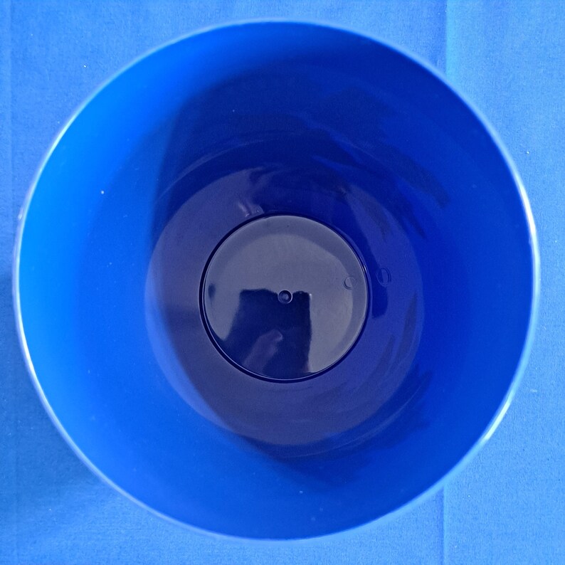 May include: A top-down view of a blue plastic container. The container is round with a dark blue interior and a lighter blue exterior. The container has a circular base and a smooth, glossy finish.