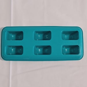Peut inclure: Un bac à glaçons turquoise avec six moules rectangulaires. Le bac est en plastique et a un bord légèrement arrondi. Les moules sont espacés uniformément et ont une légère indentation au centre.