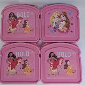 May include: Four pink lunchboxes in a bread slice shape. Each lunchbox features Disney princesses and the text "BOLD & CURIOUS". The princesses include Pocahontas, Ariel, Belle, and Rapunzel.