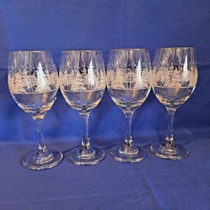 May include: Set of four clear glass wine glasses with an etched winter scene design. The glasses have a tall, slender stem and a round bowl.