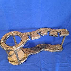 May include: Wooden wine glass and bottle holder. The holder is made of dark brown wood and has a circular section for a bottle and slots for wine glasses. The holder is designed to sit on a table or counter.