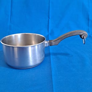 May include: A stainless steel saucepan with a black handle and a hanging loop. The pot has a shiny, reflective surface and is set against a blue background. The handle is curved for easy gripping.