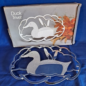 May include: A clear glass duck trivet with a silver glitter duck design, cattails, and water waves. The trivet is in a box that reads "Duck Trivet". The Wm. A. Rogers brand is visible on the box.