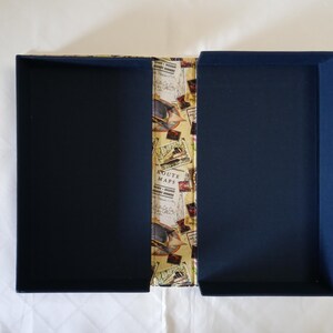 May include: Open, navy blue box with a patterned spine featuring vintage travel imagery. The interior of the box is a solid navy blue. The spine has a repeating pattern of stamps, maps, and travel-related ephemera.