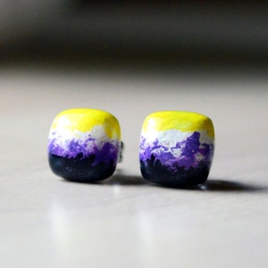 May include: A pair of square-shaped earrings with a yellow, white, and purple color scheme. The earrings are made of polymer clay and have a glossy finish.