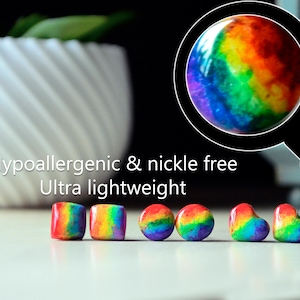 May include: A collection of colorful, rainbow-hued beads in various shapes: square, round, and heart-shaped. The image includes text that reads "Hypoallergenic & nickel free" and "Ultra lightweight". A white, spiral-patterned pot with greenery is in the background.