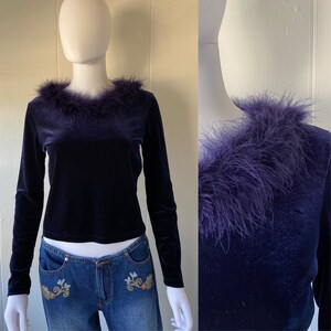May include: A dark blue velvet long-sleeve top with a purple feather trim around the neckline.