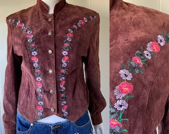 May include: A brown suede jacket with a mandarin collar and floral embroidery. The jacket has a button-up front and long sleeves.