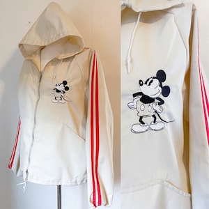 May include: A cream-colored hooded jacket with red stripes down the sleeves and a black and white embroidered Mickey Mouse on the front.