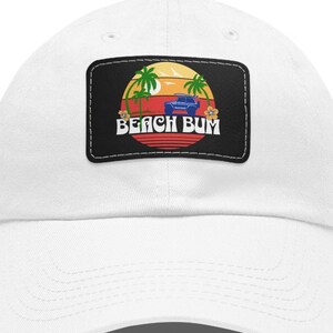 May include: White baseball cap with a black patch featuring a retro sunset scene with palm trees, a car, and the text "Beach Bum".